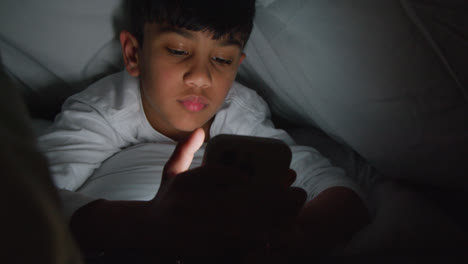 Close-Up-Of-Young-Boy-In-Bedroom-At-Home-Using-Mobile-Phone-To-Text-Message-Under-Covers-Or-Duvet-At-Night-4